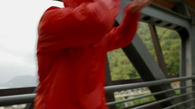 a man in a red jacket with a hood is boxing on an iron bridge. the average plan. the camera is moving