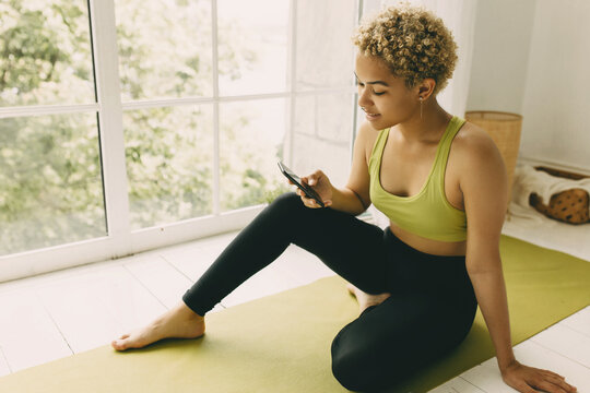 Slim Teenage Girl With Afro Hair Dyed Blonde Finished Her Yoga Exercises And Having Video Call With Fianc? On Phone, Panoramic Window Behind, Having Positive Thoughts, Feeling Good, Looking Happy