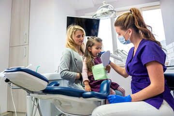 female dentist checks the patient's teeth while her mother supports her in the dental clinic.