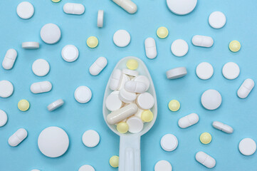 Various vitamins and nutritional supplements in a white spoon on a blue background. The concept of prevention and treatment of diseases.