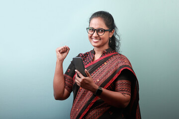 Portrait of a smiling woman of Indian ethnicity wearing sari and holding mobile phone in hand