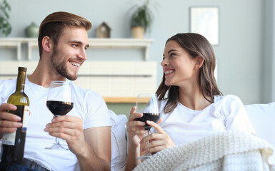 Young loving couple drinking a glass of red wine in their living room.