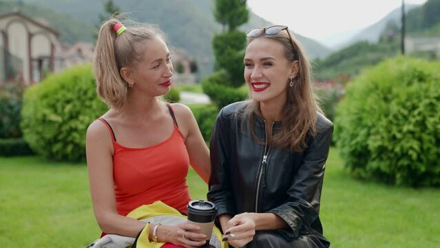portrait of two blondes with bright lipstick on the background of mountains. blondes chat, one of them smokes