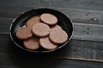 Chocolate flavored cookies Served in a black plate on a wooden table.
