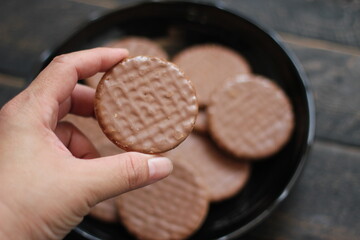 hand holding chocolate flavored cookies Served in a black plate on a wooden table.