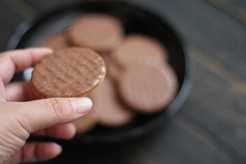 hand holding chocolate flavored cookies Served in a black plate on a wooden table.