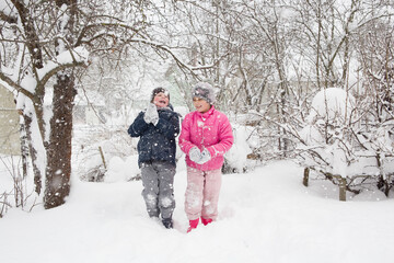 Fototapeta na wymiar Ein MÃ¤dchen und ein Junge gehen in einem verschneiten Wintergarten spazieren. es schneit stark. Es gibt kleine weiÃŸe Schneeflocken ganz Ã¼ber dem Rahmen.