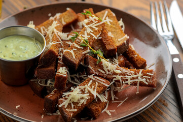 fried black bread croutons on a wooden board with sauce
