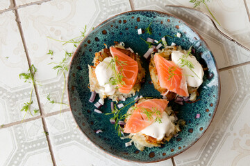 a plate of potato pancakes with salmon and sour cream on a light table