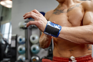 Fototapeta na wymiar Young sporty handsome man wraps his arms with gymnastic bandage getting ready for barbell exercises.