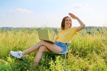 Summer vacation in wild meadow, adult woman resting on folding chair for camping using laptop