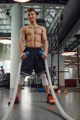 Fototapeta na wymiar Muscular powerful aggressive man training with rope in functional training fitness gym. Motion blur