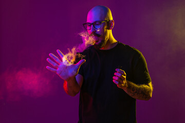 Bald man reaches for ring of smoke with his hand while blowing smoke. color filters. Vaping concept