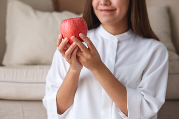 Closeup image of a young woman holding a red apple at home