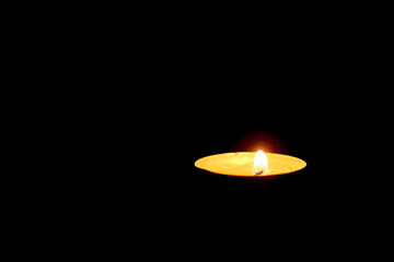 Round candle. floating candles in an aluminum stake. aluminum burning tea candle isolated on a black background. Low light atmosphere.One candle burning on a dark background of sorrow and memory