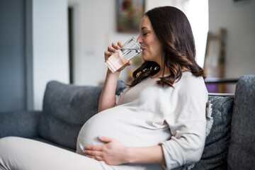 Pregnant woman relaxing at home. She is sitting on bed and drinking water.
