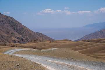Fototapeta na wymiar Gravel road in the mountains with sky background. Road to Bartogay reservoir from Assy plateau.