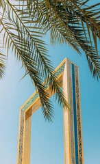 Foto op Plexiglas Vertical High quality photo. View Of Dubai Frame On Sunny Blue Sky Under Palm Branches. Dubai Frame Is Architectural Landmark In Zabeel Park, Dubai. It Holds Record For Largest Frame In The World © Grigory Bruev