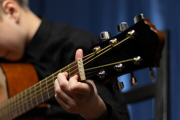 A teenager guy in a black shirt plays the acoustic guitar at a concert on a blue background. Hobby. Musical instruments. Selective focus. Portrait