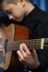 Fototapeta na wymiar A teenager guy in a black shirt plays the acoustic guitar at a concert on a blue background. Hobby. Musical instruments. Selective focus. Portrait
