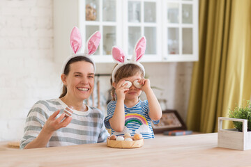 Happy easter! Happy family preparing for Easter. mom and cute child girl wears rabbit ears holds a basket with painted eggs in the kitchen of the house.