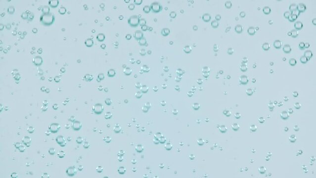 Macro shot of air bubbles in water rising up on light blue background. Slow motion. High quality FullHD footage