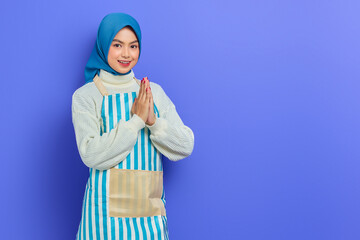 Smiling young Asian Muslim woman in 20s wearing hijab and apron, open sign to greet and greet customers isolated on purple background. People housewife muslim lifestyle concept