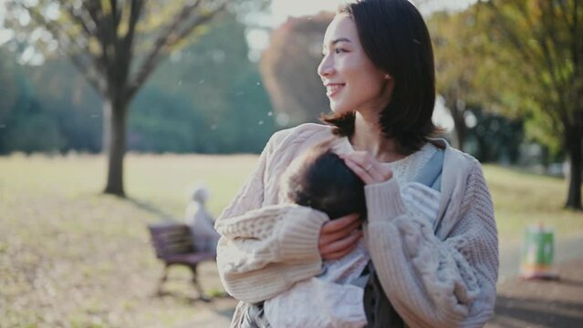 赤ちゃんを抱っこして夕暮れの公園を歩くお母さん