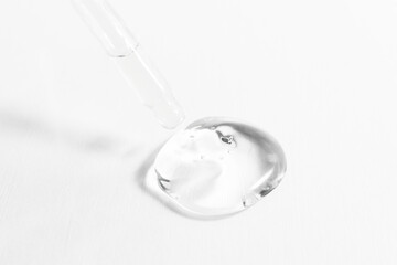 Fototapeta na wymiar A drop of transparent cosmetic gel on a white background with a glass dropper, close-up. Beauty treatments with hyaluronic acid to moisturize and maintain skin elasticity.
