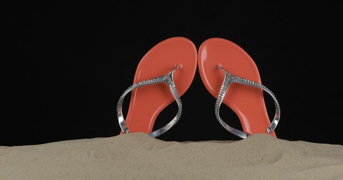 Pair of pink flip flops embellished with rhinestones stick out of the sand. Slider shot. Isolated