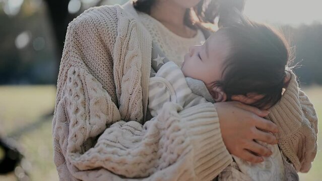 眠る赤ちゃんを抱っこして散歩するお母さん