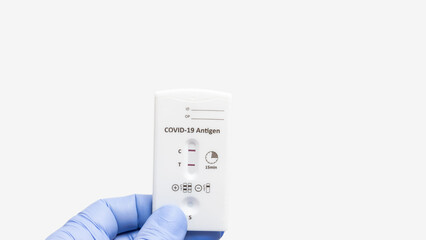 Hand in a medical glove holds rapid antigen test kit for viral disease COVID-19 with positive result, white background with copy space