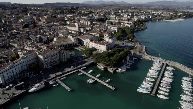 Aerial image filmed with a drone showing the town of Desenzano del Garda located on the shores of Lake Garda, northern Italy. Small port with sailing boats. Boats and yachts on the lake.