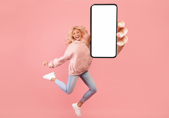 Excited lady showing empty cellphone screen while jumping up on pink studio background, collage,...