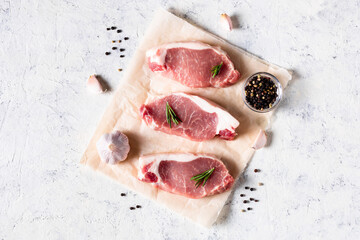 A pieces of raw fresh pork with rosemary and garlic on a vax paper on white background. Meat with...