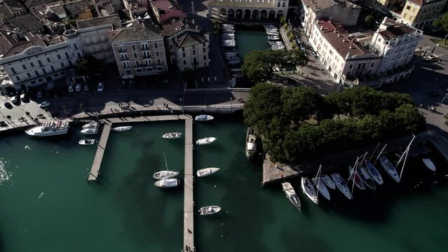 Aerial image filmed with a drone showing the town of Desenzano del Garda located on the shores of Lake Garda, northern Italy. Small port with sailing boats. Boats and yachts on the lake.