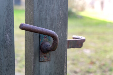 Nahaufnahme eines Details eines alten Holztores mit rostiger Klinke und Drücker aus massivem Eisen und Blick in den Garten im verschwommenen Hintergrund, selektiver Fokus