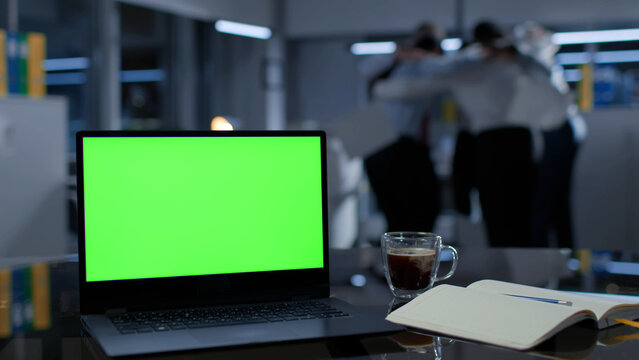 Focus on laptop with green screen on desk in office. Business tean celebrating success - Powered by Adobe