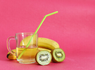 ripe kiwi in a banana section and a cup with juice on a pink background