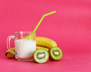 ripe kiwi in a banana section and a cup of milk on a pink background