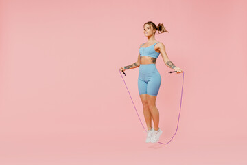 Full size young sporty athletic fitness trainer instructor woman wear blue tracksuit spend time in home gym using skipping rope isolated on pastel plain light pink background. Workout sport concept.