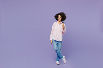 Full body young woman of African American ethnicity wear pink striped shirt hold takeaway delivery craft paper brown cup coffee to go isolated on plain pastel light purple background studio portrait.