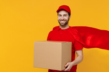 Professional minded delivery guy employee man 20s in red cap T-shirt uniform red cloak workwear work as dealer courier hold cardboard box isolated on plain yellow background studio Service concept