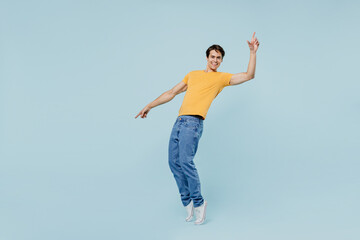 Full body smiling happy cool young man 20s wear yellow t-shirt leaning back stand on toes dance fooling around isolated on plain pastel light blue background studio portrait. People lifestyle concept.