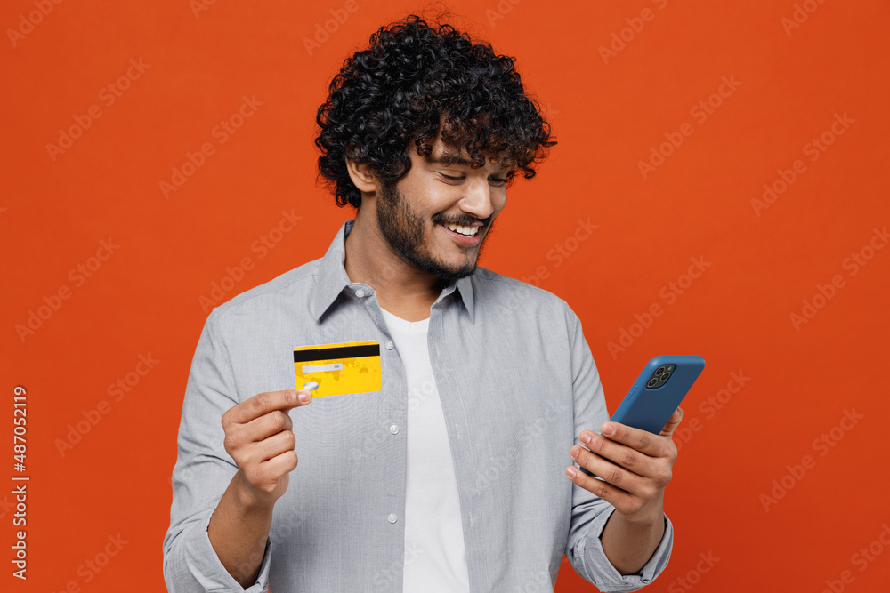 Wall mural smiling young bearded indian man 20s years old wears blue shirt using mobile cell phone hold credit 