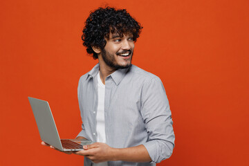 Smiling young bearded Indian man 20s years old wear blue shirt hold use work on laptop pc computer...