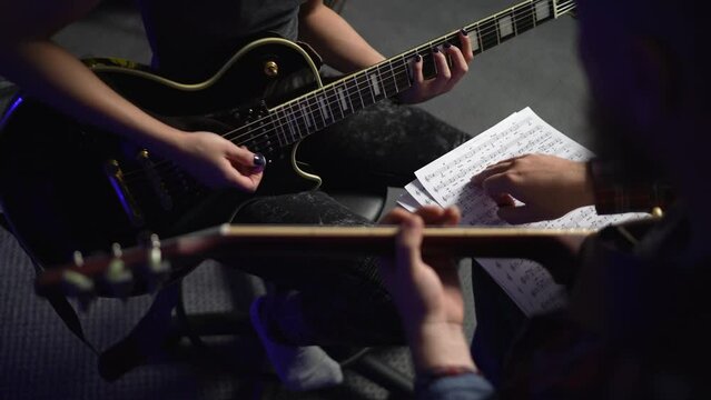 Musicians rehearse on guitars in studio, guitarist put notes of new song on his knees and together with a friend they disassemble chords and try to play it. Rock and roll playing on Jazz guitar