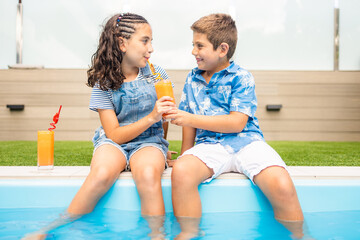 Two little kids sharing an orange juice in the swimming pool