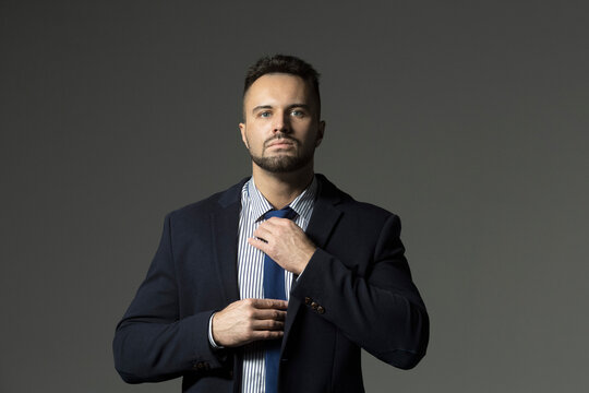 Portrait confident, handsome businessman adjusting necktie against black background
