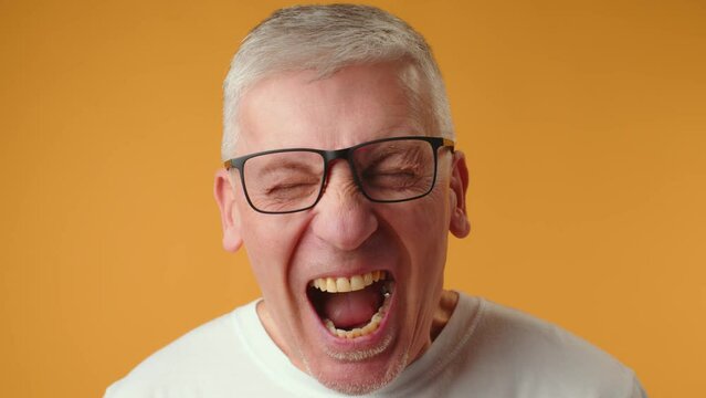 Mature elderly man screaming loud against yellow background